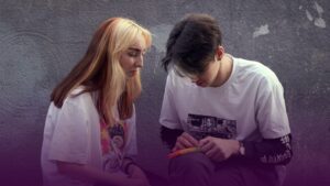 Two young white people sitting together looking at a mobile phone.