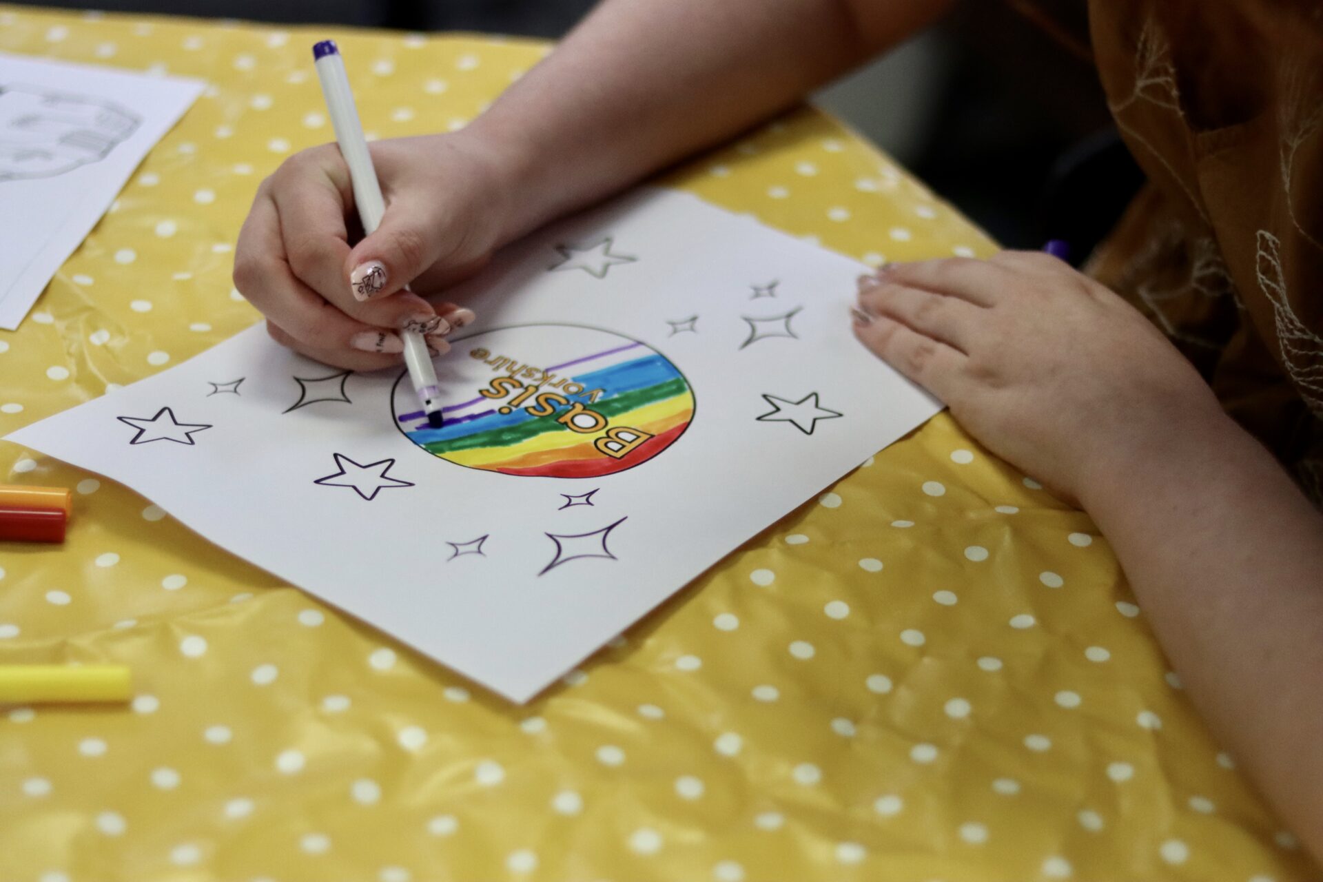 Close up of a person's hands colouring in the Basis Yorkshire logo with rainbow colours.